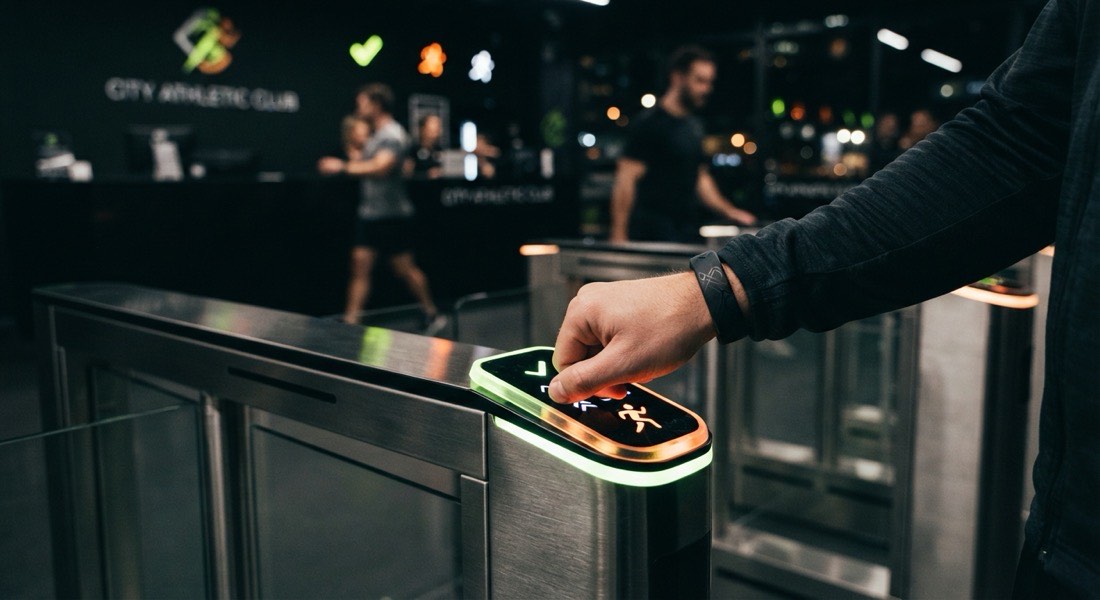 Member tapping a card at a glowing turnstile reader at a sports club entrance at night